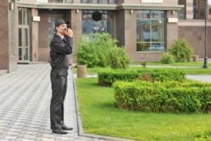 security guard solution| a guard in his uniform monitoring the building while talking on his walkie talkie